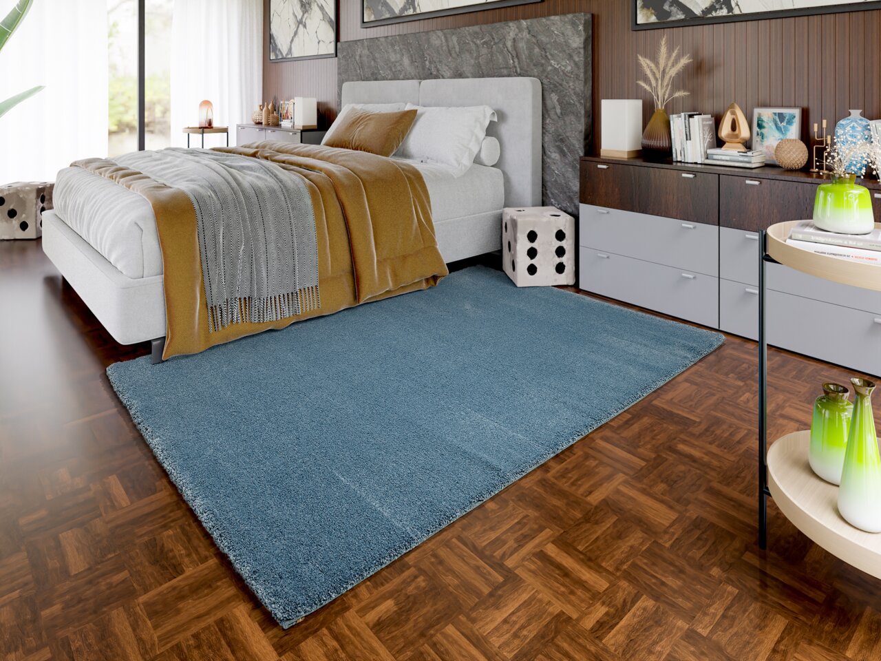 Blauer Uni-Teppich in einem modernen Schlafzimmer mit Holzboden, neben einem Bett und einer Kommode. Perspektive von schräg oben.