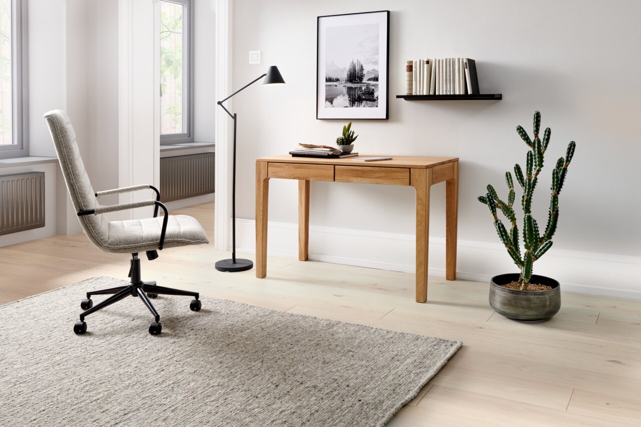 Moderner Schreibtisch aus Holz in einem stilvollen Büro mit einem ergonomischen Bürostuhl, einer Stehlampe und einem Kaktus. Perspektive von der Seite.