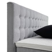 Seitliche Ansicht eines grauen Boxspringbetts mit gestepptem Kopfteil und schwarzem Kissen.