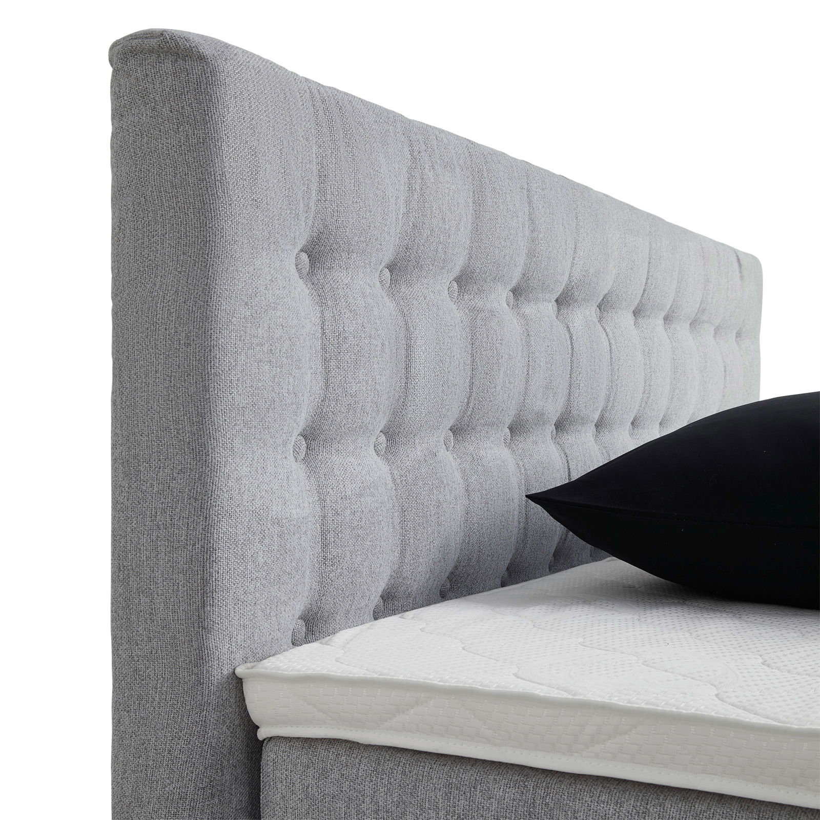 Seitliche Ansicht eines grauen Boxspringbetts mit gestepptem Kopfteil und schwarzem Kissen.