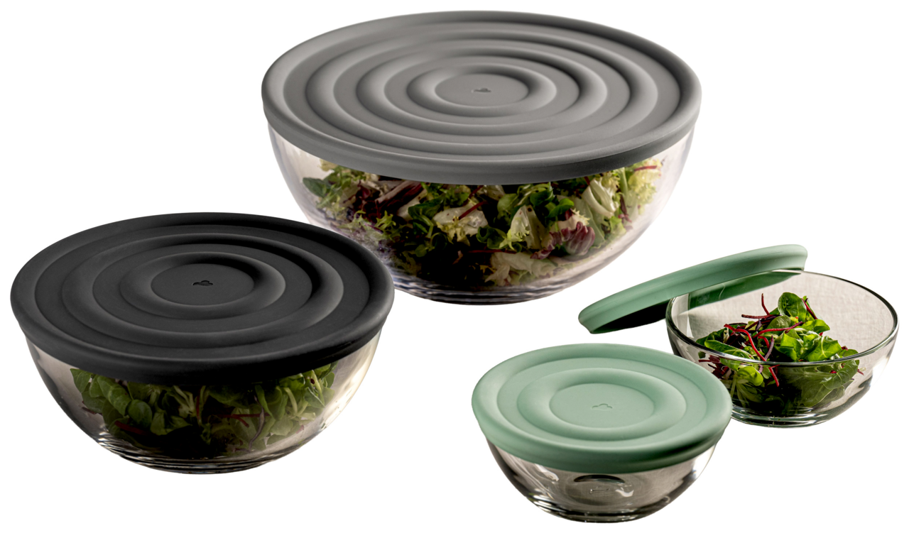 Drei Glasschalen mit Deckeln in verschiedenen Farben, gefüllt mit frischem Salat, aus einer seitlichen Perspektive fotografiert.