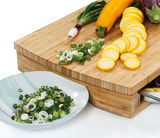 Holz-Arbeitsbrett mit geschnittenem Gemüse, darunter Frühlingszwiebeln und gelbe Zucchini, aus der Perspektive von oben rechts.