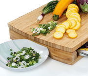 Holz-Arbeitsbrett mit geschnittenem Gemüse, darunter Frühlingszwiebeln und gelbe Zucchini, aus der Perspektive von oben rechts.