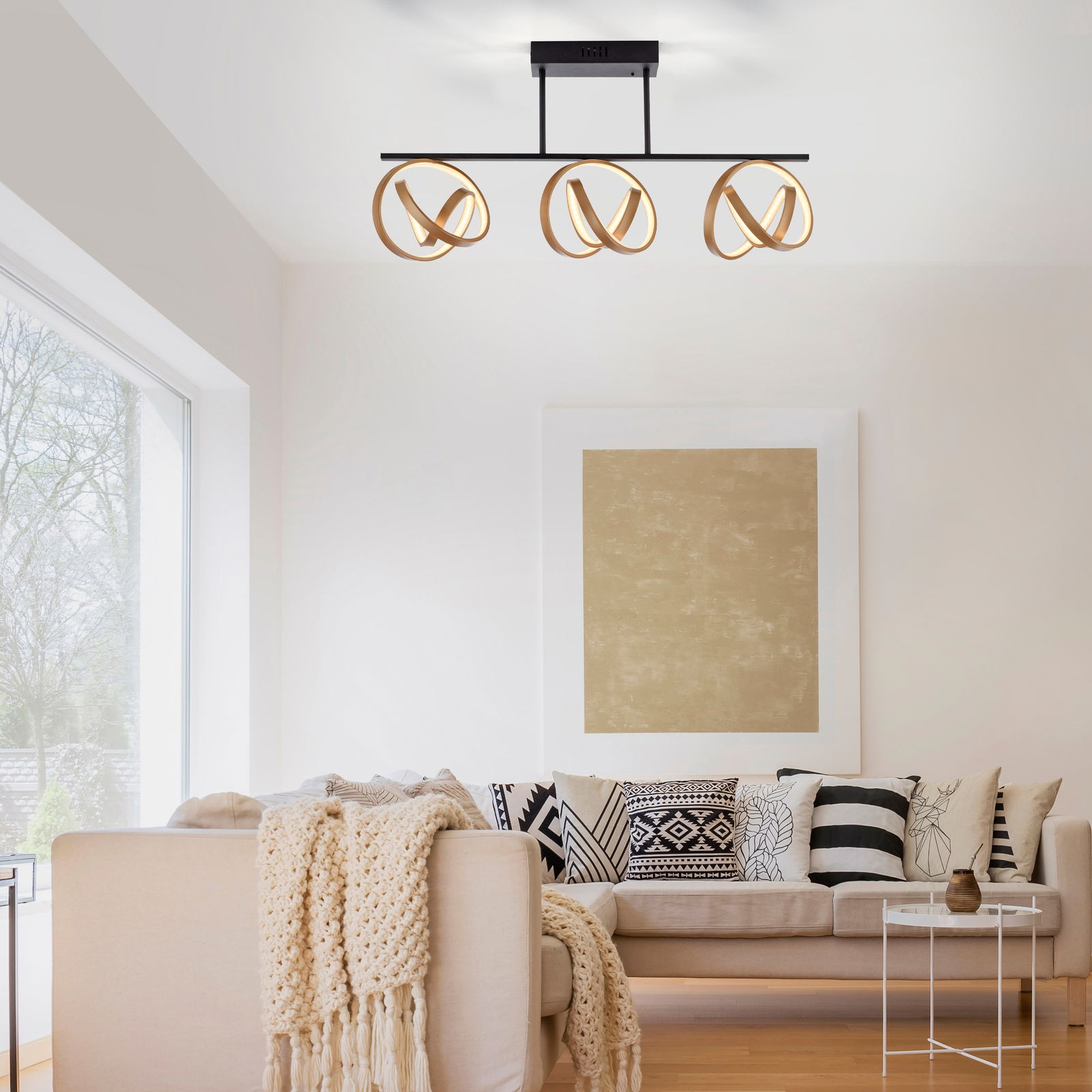 Moderne Deckenleuchte mit drei goldenen Ringen in einem stilvollen Wohnzimmer, seitliche Perspektive.