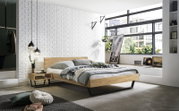 Moderne slaapkamer met een bedframe van hout en metaal, gezien vanaf de zijkant. De kamer is licht en stijlvol ingericht met grote ramen die veel daglicht binnenlaten.