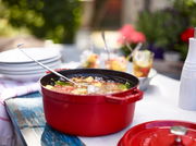 Rote runde Bräter Cocotte 24cm auf einem Tisch im Freien, gefüllt mit Suppe, seitliche Perspektive