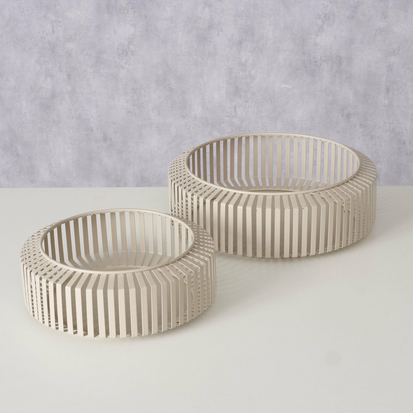 Zwei moderne, runde Schalen aus beigem Metall mit einem offenen, lamellenartigen Design, auf einer weißen Oberfläche aus der Vogelperspektive fotografiert.