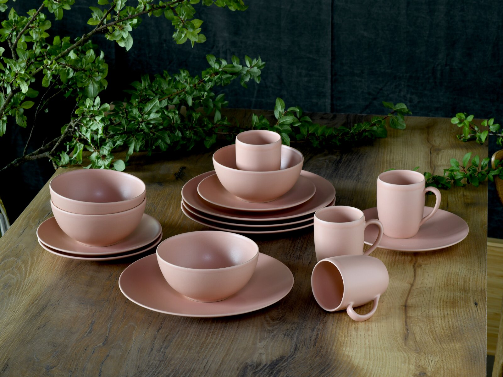 Creatable Kombiservice 16-tlg SOFT TOUCH Roséfarbenes, mattes Keramik-Geschirrset mit Tellern, Schalen und Bechern auf rustikalem Holztisch, fotografiert in leicht erhöhter Schrägansicht von vorn.