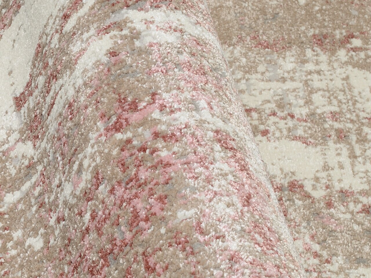 Nahaufnahme eines Designer-Teppichs mit abstraktem Muster in Beige, Rosa und Weiß, aus seitlicher Perspektive.