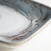Detailaufnahme einer rechteckigen Keramikschale mit blau-grauer, marmorierter Glasur und braunen Akzenten, fotografiert aus schräger Draufsicht.