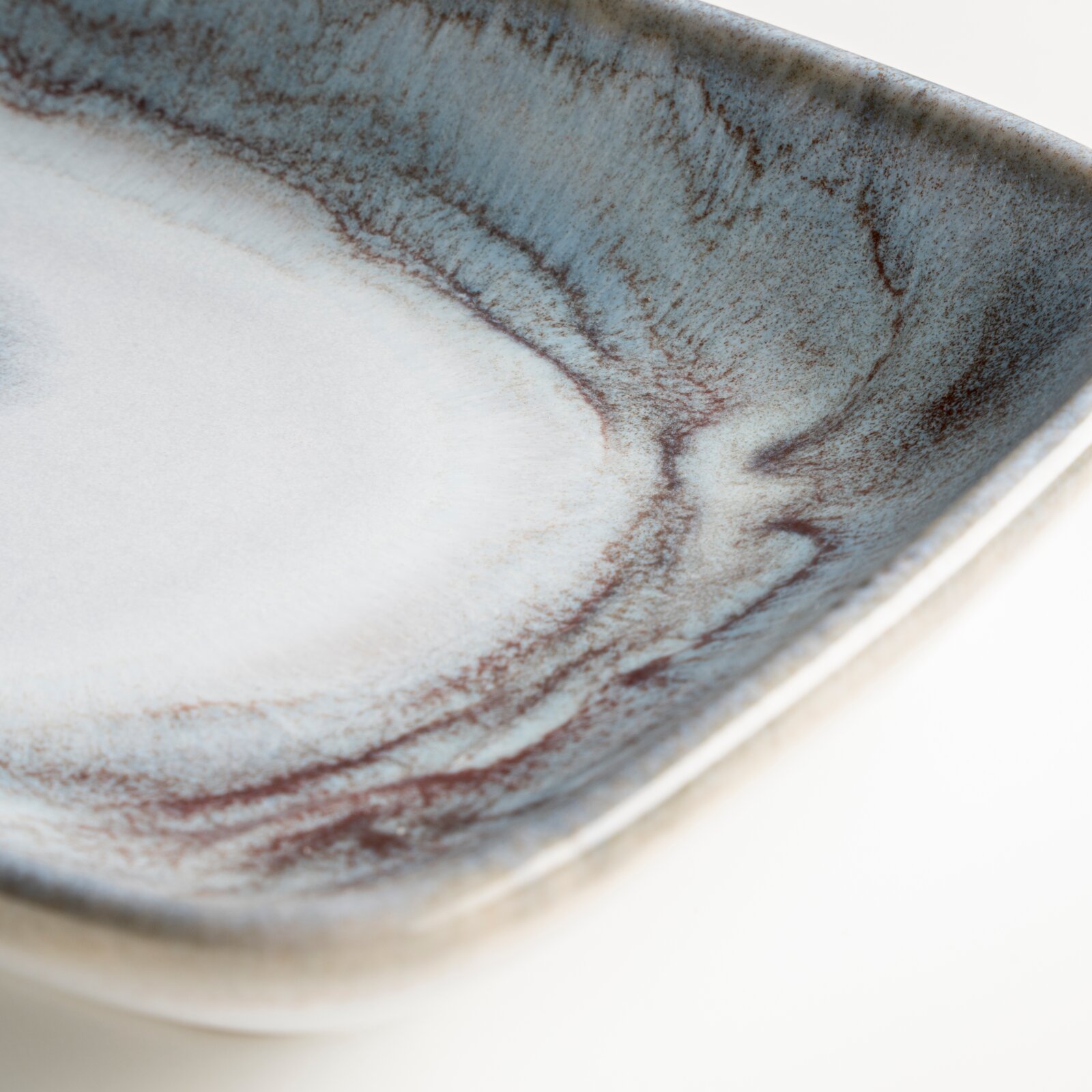 Detailaufnahme einer rechteckigen Keramikschale mit blau-grauer, marmorierter Glasur und braunen Akzenten, fotografiert aus schräger Draufsicht.