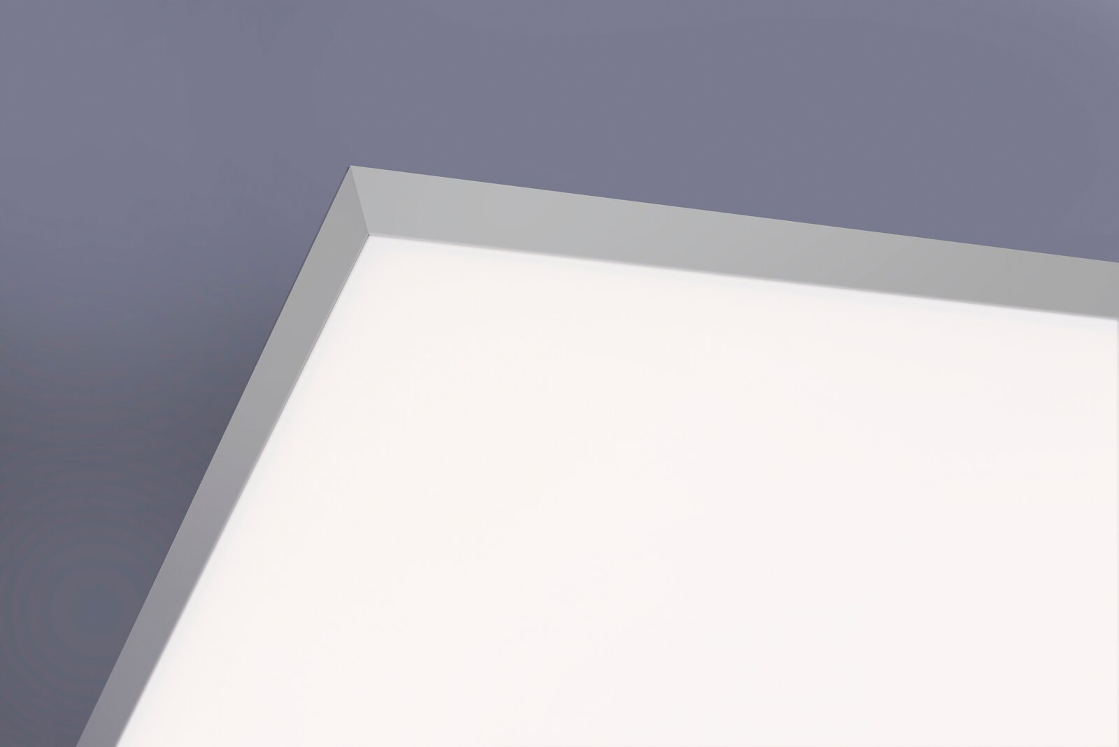Weiße, flache LED-Deckenleuchte mit silbernem Rahmen, Nahaufnahme aus schräger Untersicht auf die Ecke der Leuchte vor grauem Hintergrund