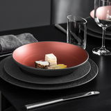 Elegante Schale mit rotem Innenbereich, gefüllt mit feinem Essen, auf einem gedeckten Tisch von oben betrachtet.