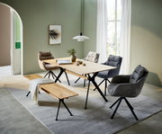 Moderne eettafel met houten blad en zwarte metalen poten, omringd door gestoffeerde stoelen en een houten bank, in een lichte ruimte met groene muren en grote ramen, zijaanzicht.