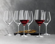 Sechs elegante Bordeauxkelche der Serie Topline, teilweise mit Rotwein gefüllt, auf einer grauen Oberfläche vor einem stilvollen Hintergrund, seitliche Perspektive.