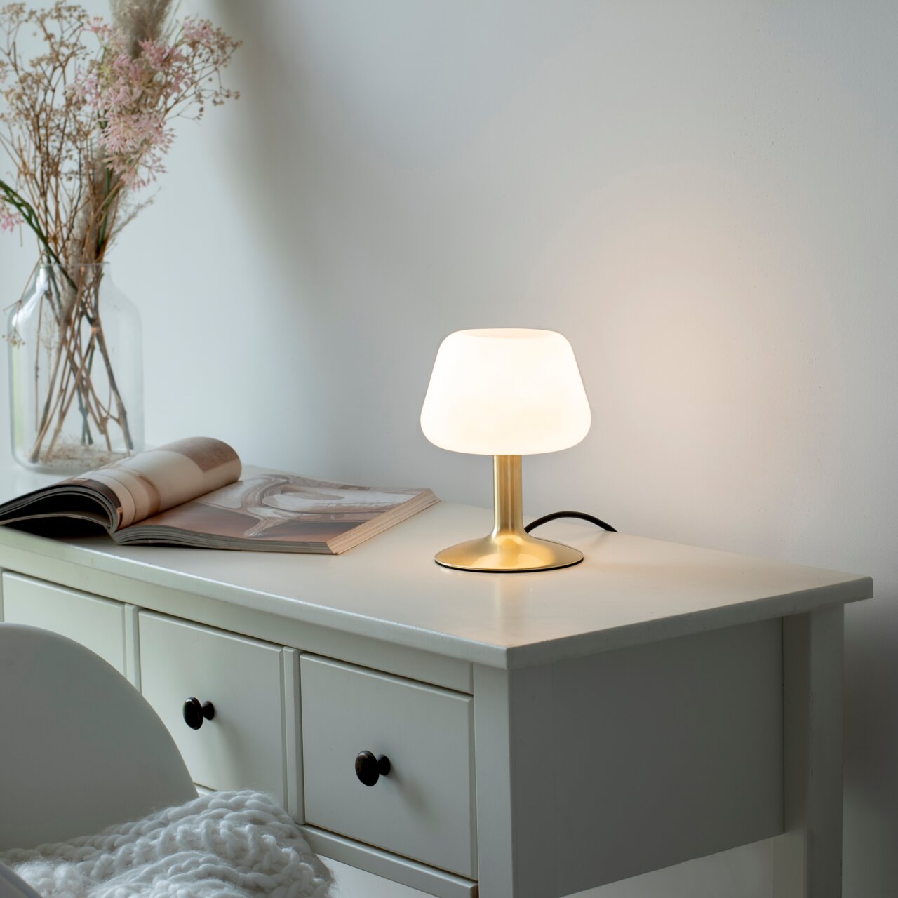 Tafellamp van mat messing op een witte tafel, zijaanzicht