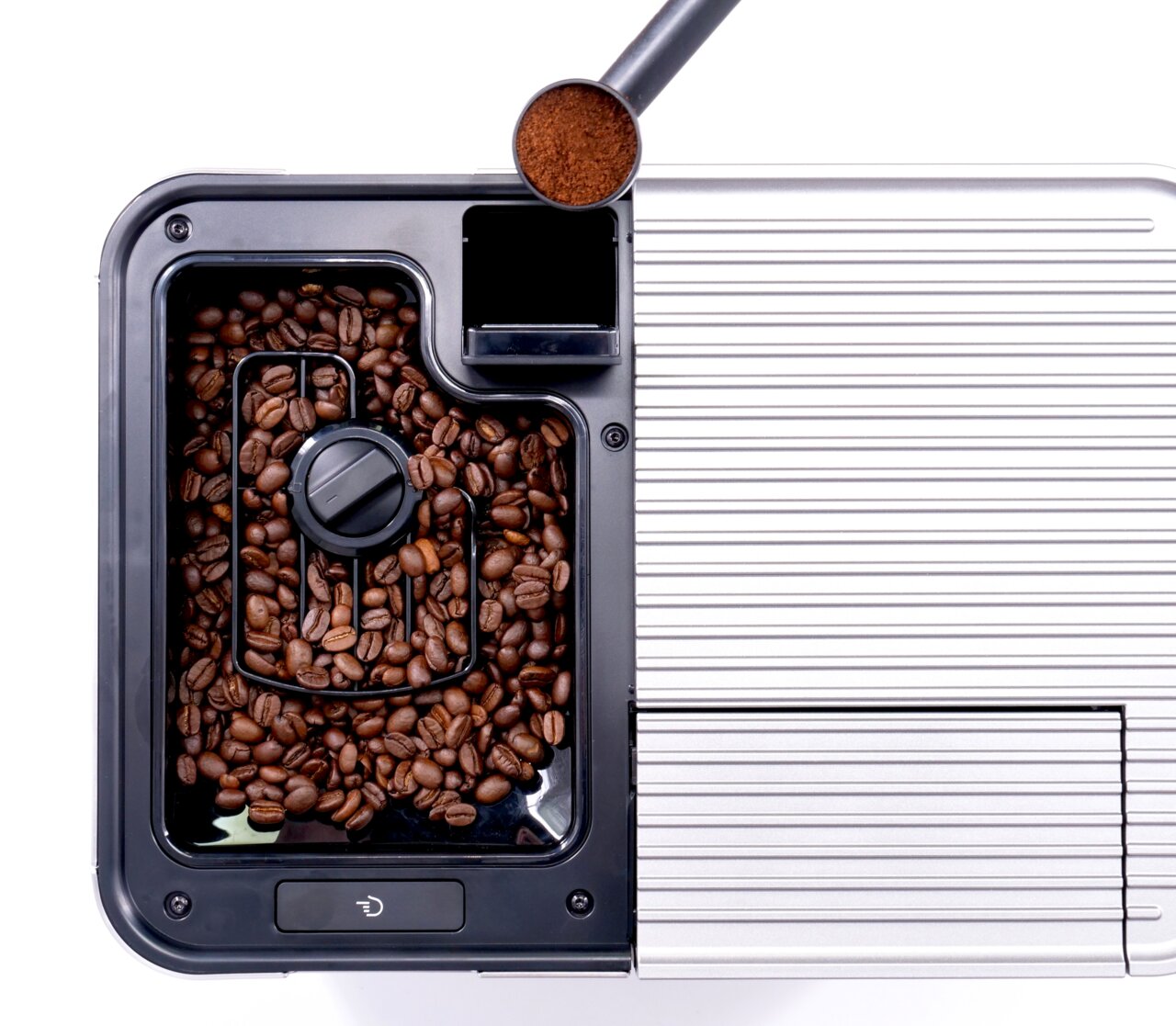 Draufsicht auf einen Kaffeevollautomaten mit Kaffeebohnenbehälter und Kaffeepulver im Messlöffel.