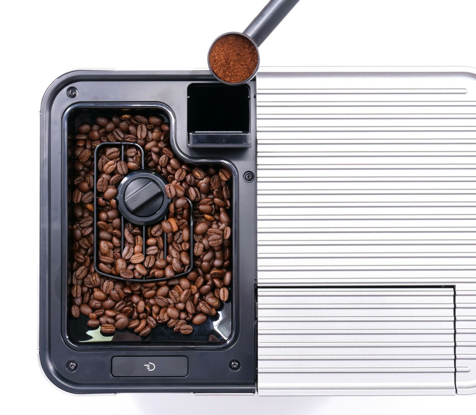 Draufsicht auf einen Kaffeevollautomaten mit Kaffeebohnenbehälter und Kaffeepulver im Messlöffel.