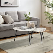 Modernes Couchtisch-Set mit zwei runden Tischen, Marmoroptik und schwarzen Beinen, im Wohnzimmer mit grauem Sofa und Pflanzen, seitliche Perspektive.