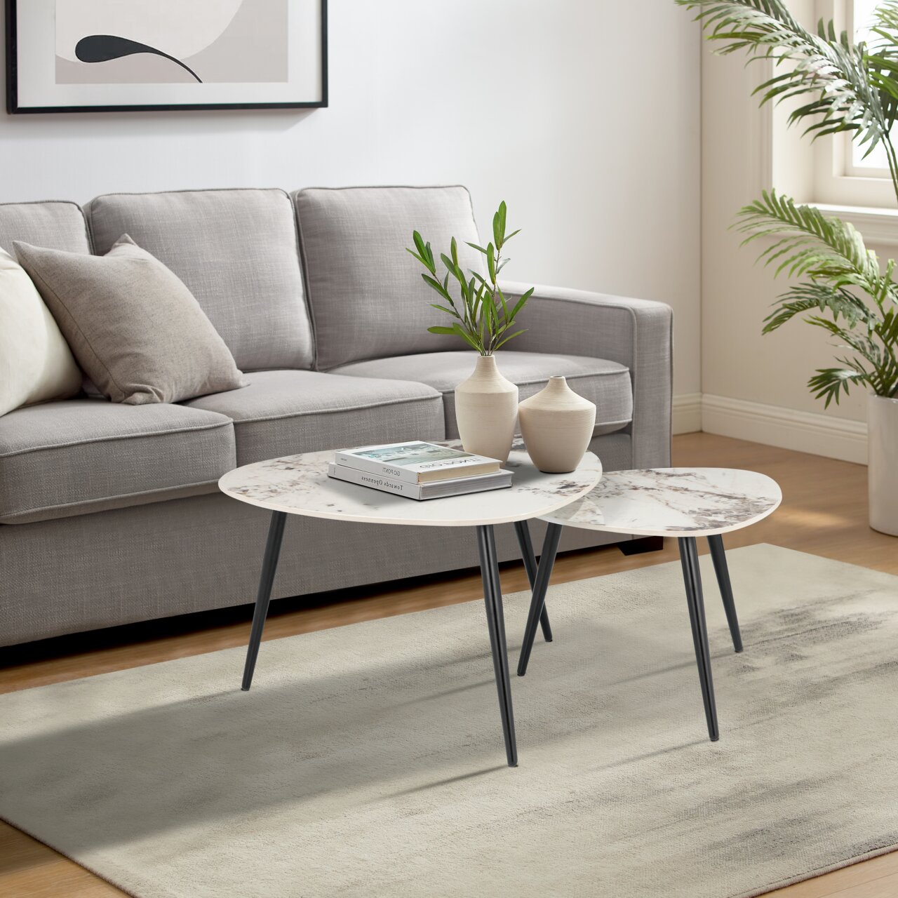 Modernes Couchtisch-Set mit zwei runden Tischen, Marmoroptik und schwarzen Beinen, im Wohnzimmer mit grauem Sofa und Pflanzen, seitliche Perspektive.