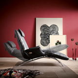 Elegante Funktionsliege Koinor JOLEEN in schwarzem Leder, seitliche Perspektive, vor roter Wand mit moderner Kunst.