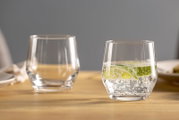 Twee doorzichtige bekers op een tafel, waarvan één gevuld met bruisend water en schijfjes limoen, gezien vanuit de zijkant.