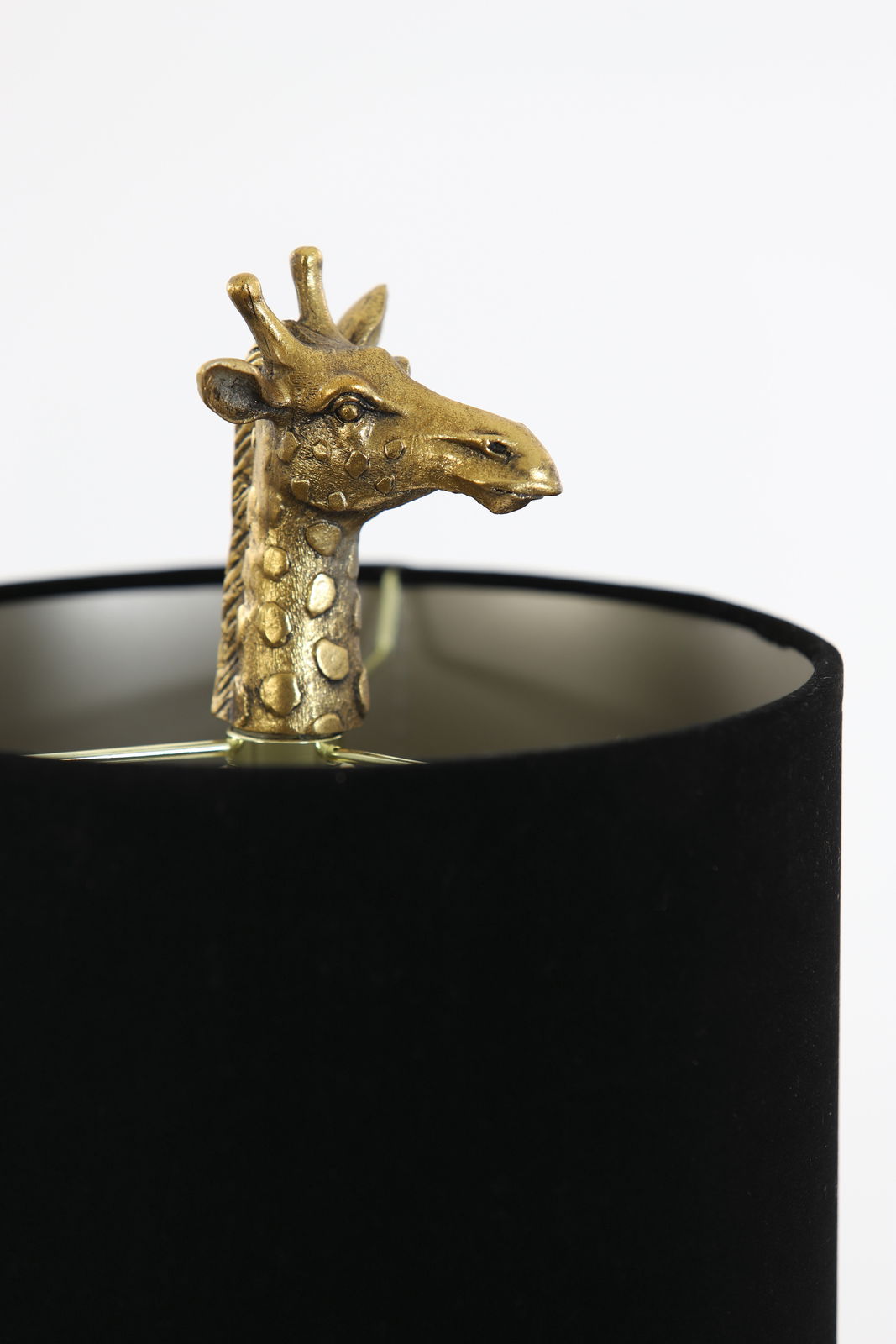 Nahaufnahme einer Tischleuchte mit einer goldenen Giraffenskulptur, die aus einem schwarzen Lampenschirm herausragt.