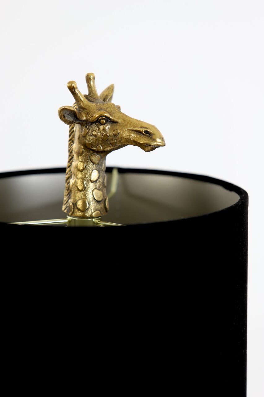Close-up van een tafellamp met een gouden girafbeeldje dat uit een zwarte lampenkap steekt.