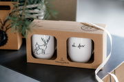 Zwei weiße Tassen in einer Geschenkverpackung mit Rentier- und 'oh deer'-Motiv, seitliche Perspektive