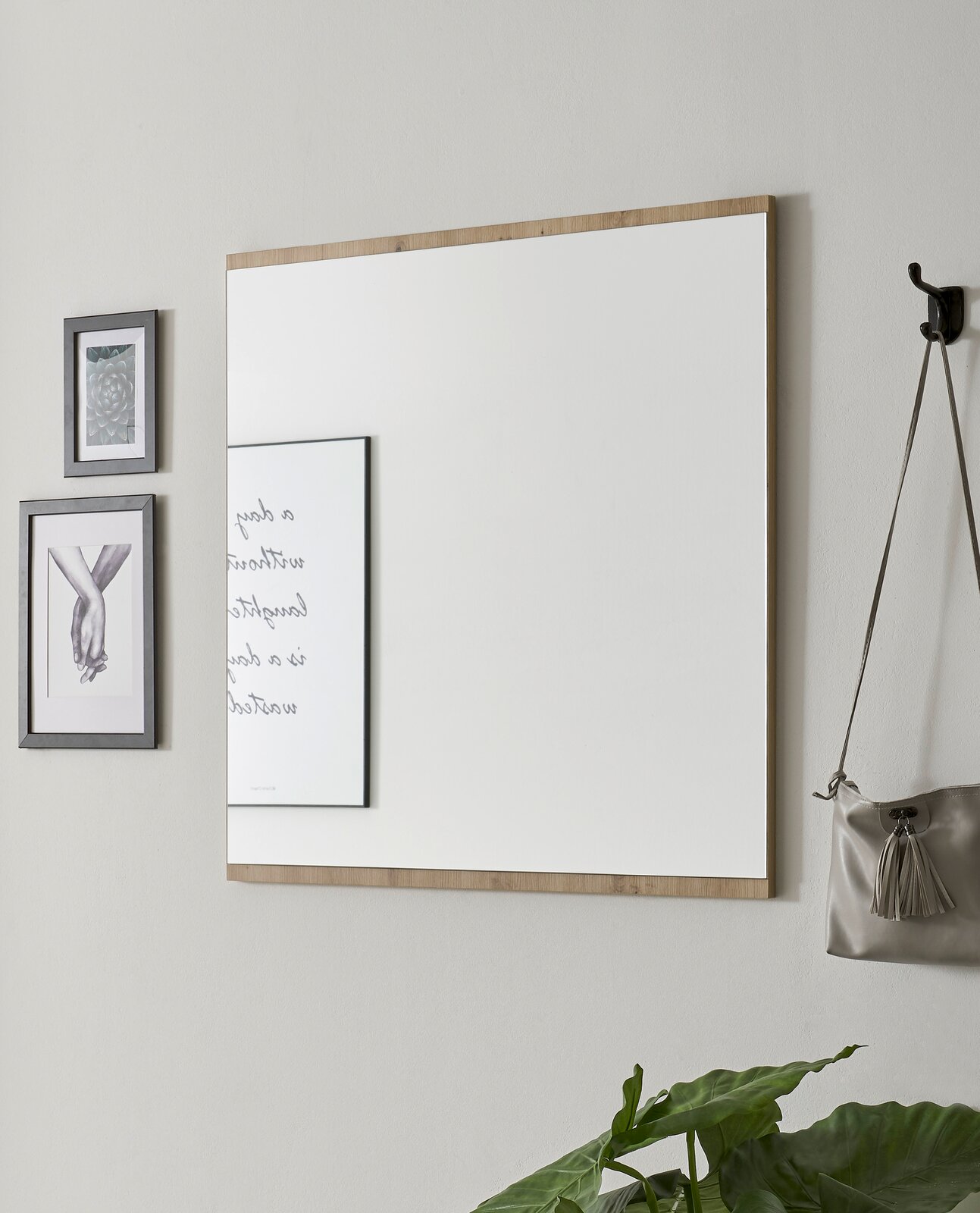 Rechteckiger Wandspiegel mit Holzrahmen, seitliche Perspektive, neben dekorativen Bildern und einer Tasche an der Wand.