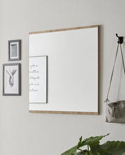 Rechteckiger Wandspiegel mit Holzrahmen, seitliche Perspektive, neben dekorativen Bildern und einer Tasche an der Wand.