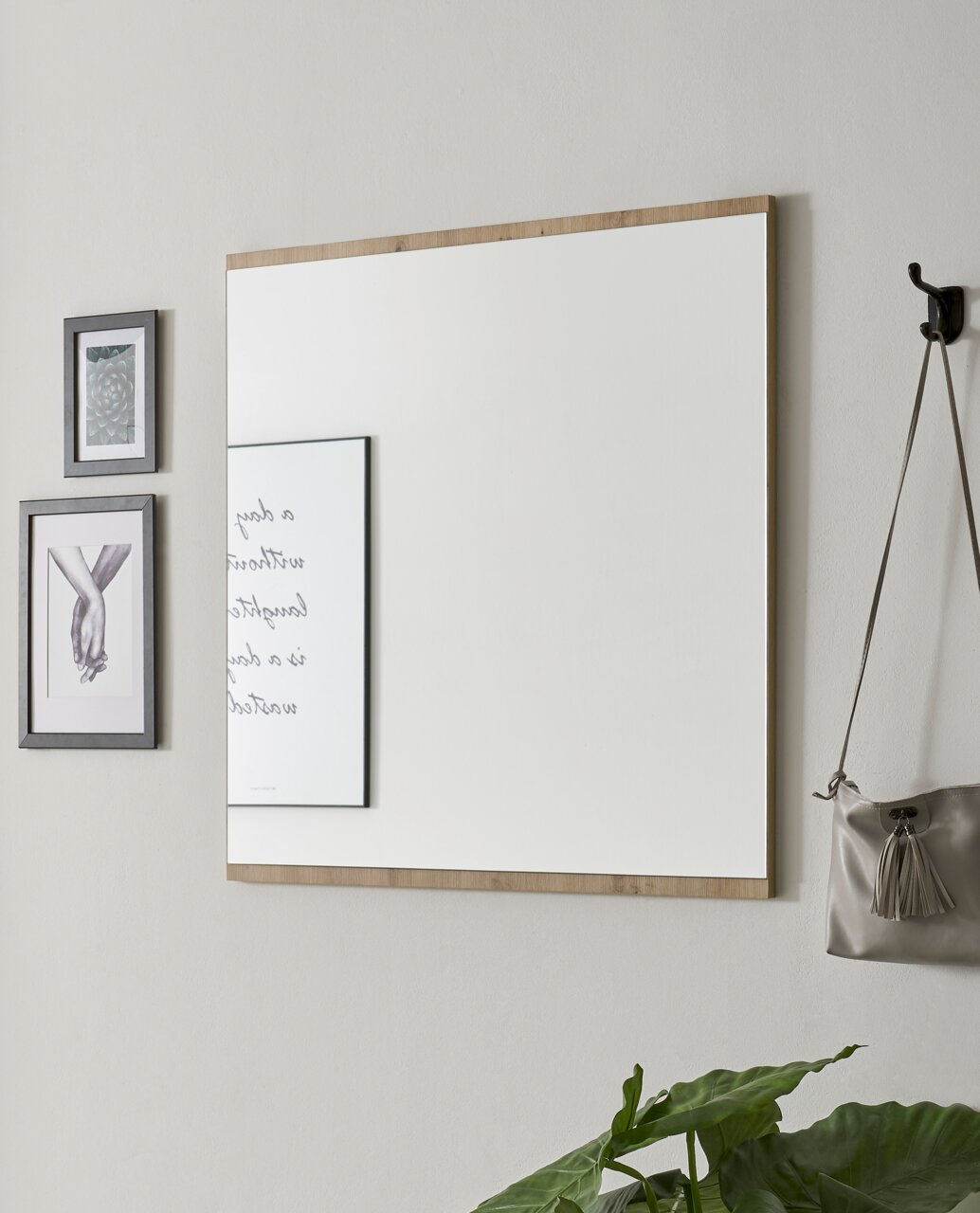 Rechteckiger Wandspiegel mit Holzrahmen, seitliche Perspektive, neben dekorativen Bildern und einer Tasche an der Wand.