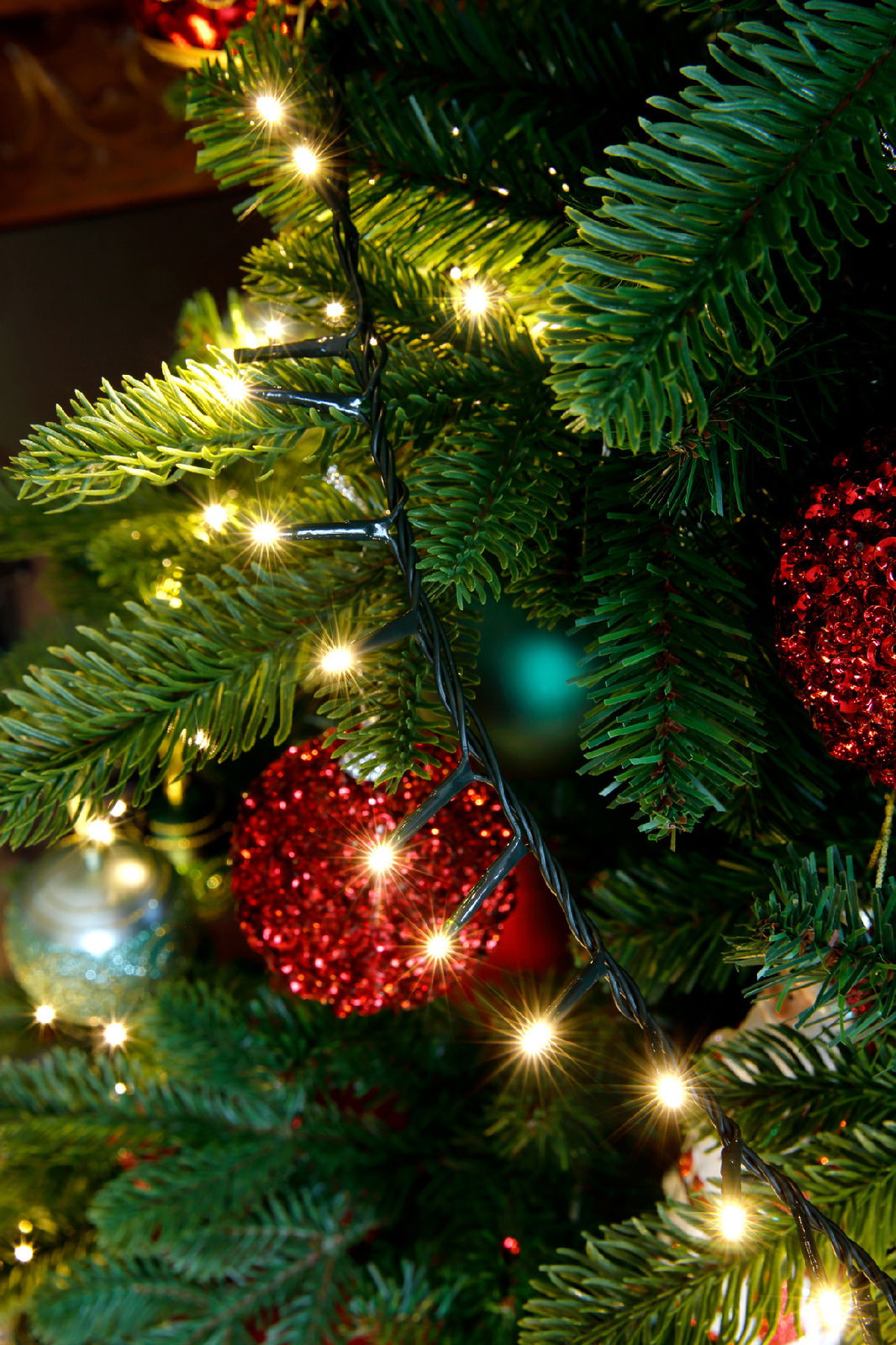 Nahaufnahme eines Weihnachtsbaums mit leuchtenden LED-Lichtern und roten Kugeln, seitliche Perspektive.