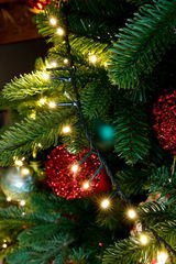 Nahaufnahme eines Weihnachtsbaums mit leuchtenden LED-Lichtern und roten Kugeln, seitliche Perspektive.