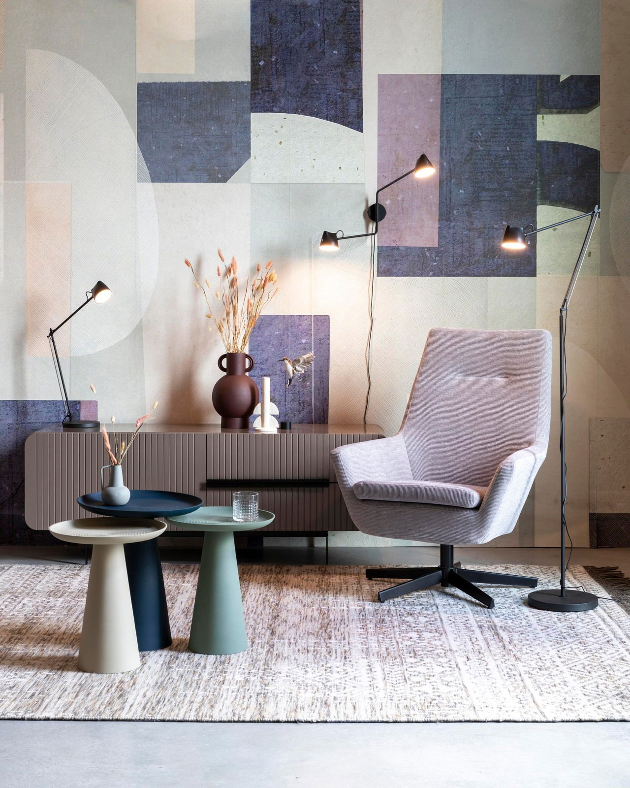 Moderne Beistelltische in verschiedenen Farben vor einer stilvollen Wohnzimmerkulisse mit Sessel und Stehlampen, seitliche Perspektive.