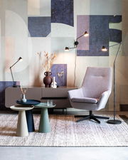 Moderne Beistelltische in verschiedenen Farben vor einer stilvollen Wohnzimmerkulisse mit Sessel und Stehlampen, seitliche Perspektive.