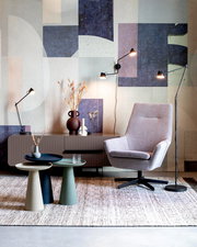 Moderne Beistelltische in verschiedenen Farben vor einer stilvollen Wohnzimmerkulisse mit Sessel und Stehlampen, seitliche Perspektive.