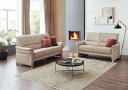Modernes Wohnzimmer mit zwei beigen 2,5-Sitzer Sofas, einem runden Couchtisch und einem Kamin im Hintergrund, seitliche Perspektive.