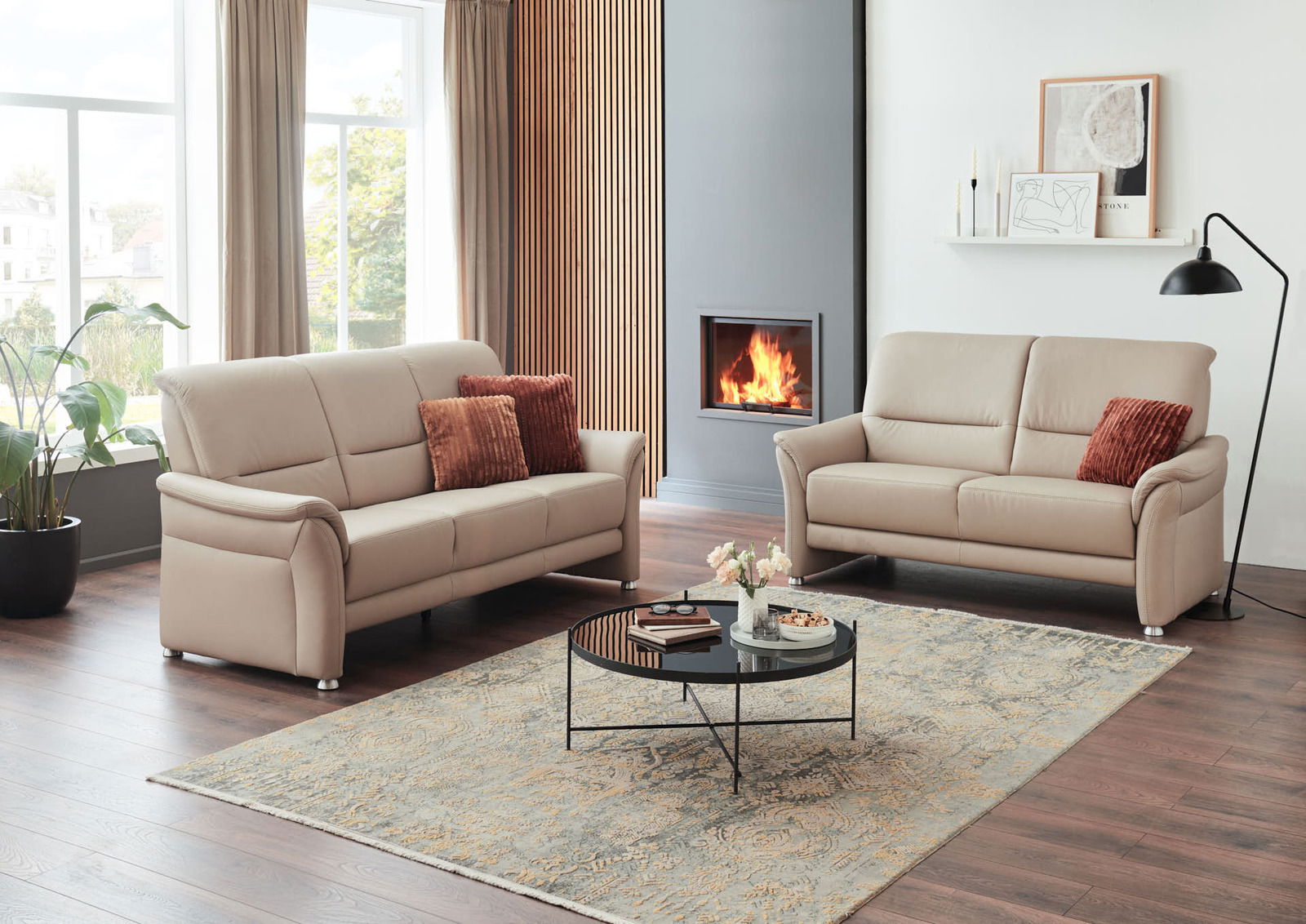 Modernes Wohnzimmer mit zwei beigen 2,5-Sitzer Sofas, einem runden Couchtisch und einem Kamin im Hintergrund, seitliche Perspektive.