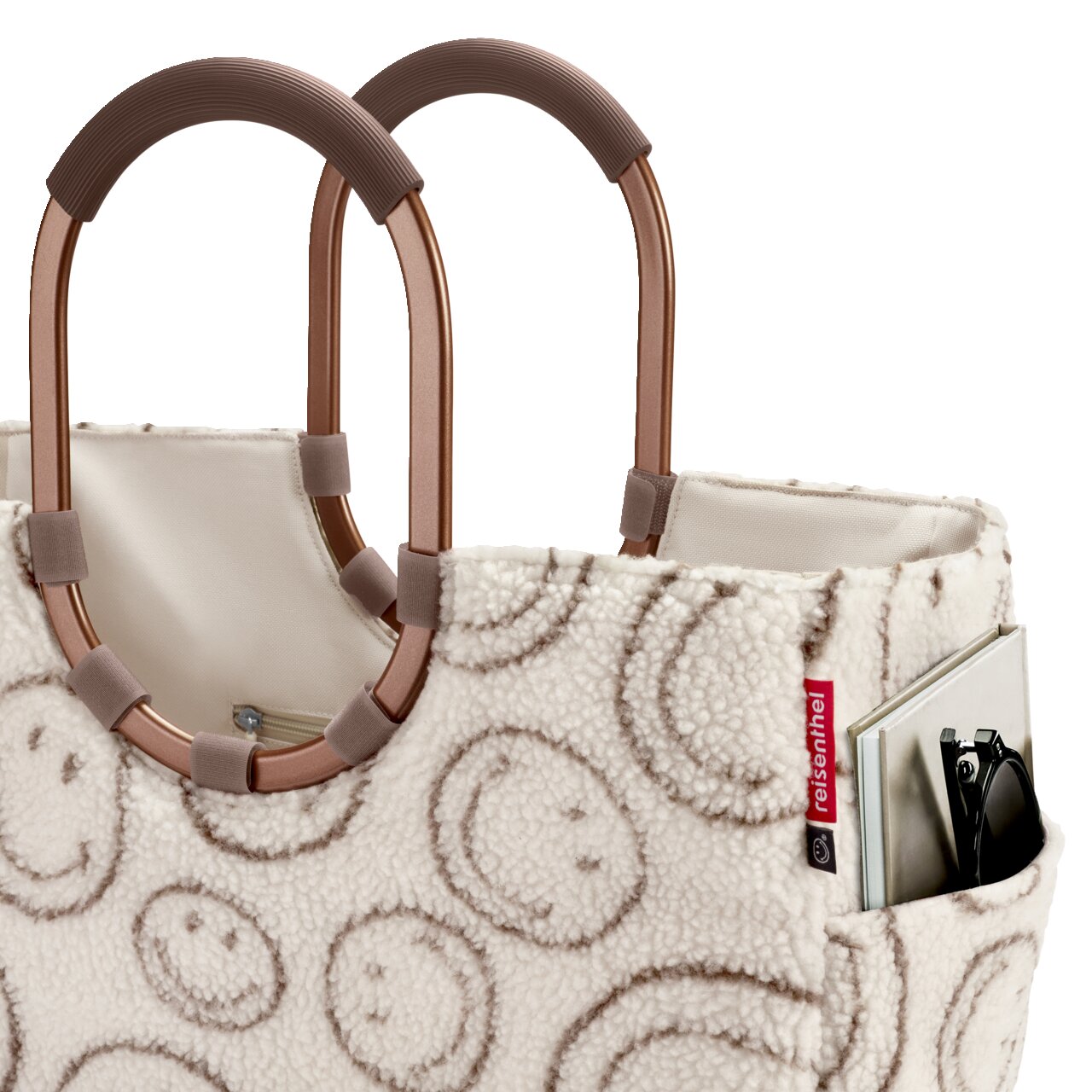 Reisenthel Shopper-Tasche aus cremefarbenem Teddyplüsch mit Kreis-Muster, braunen Tragegriffen und seitlicher Außentasche mit Buch und Sonnenbrille, Nahaufnahme in leichter Schrägansicht von vorn