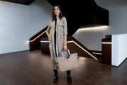 Frau in modernem Innenraum hält eine beige Tasche mit runden Griffen, seitliche Perspektive.
