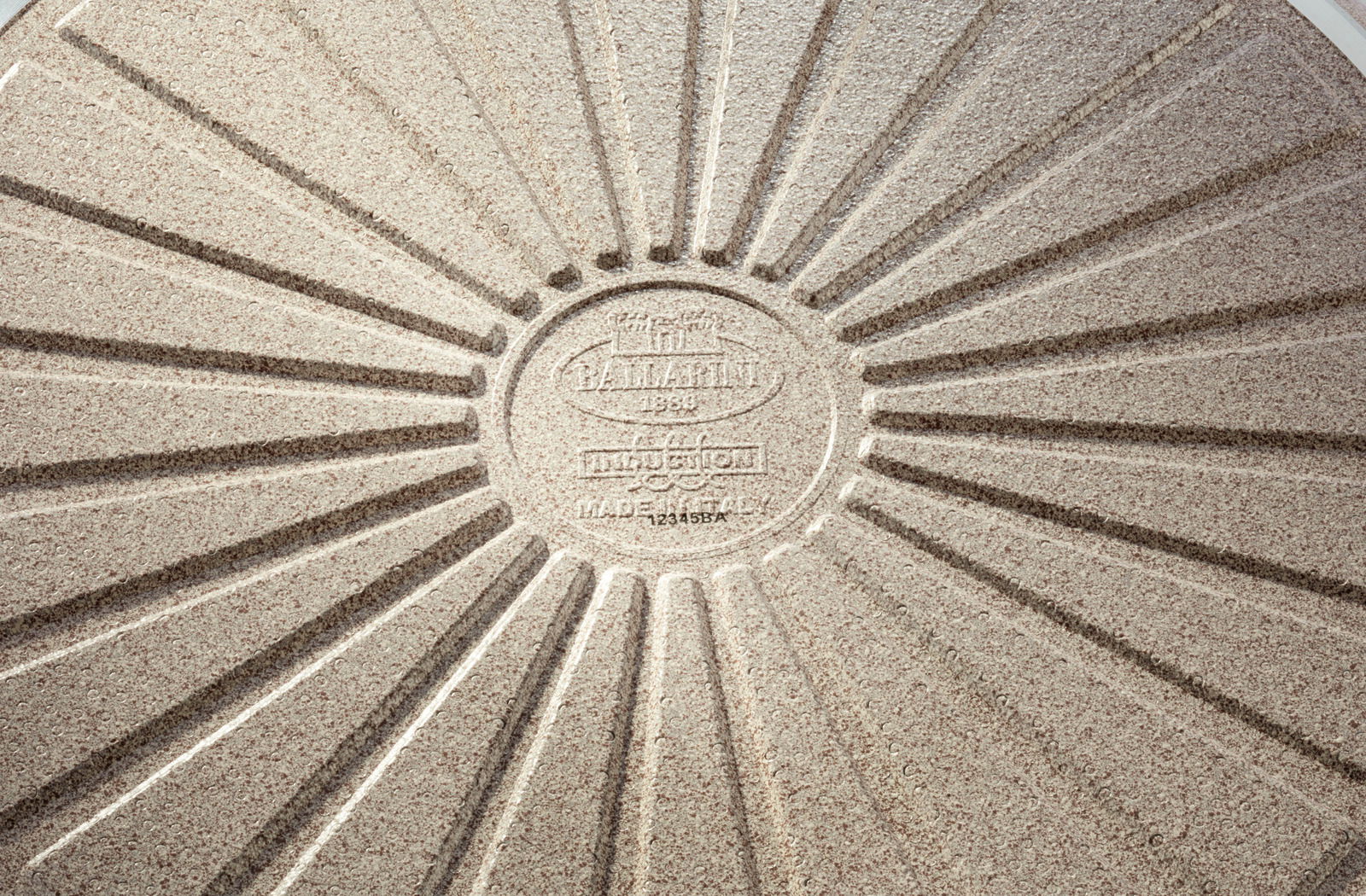 Unterseite einer Bratpfanne mit radialem Rillenmuster und Prägung, Draufsicht