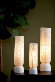 Vooraanzicht van drie slanke tafellampen in verschillende hoogtes, met transparante geribbelde kappen, warm licht en witte ronde voetstukken.
