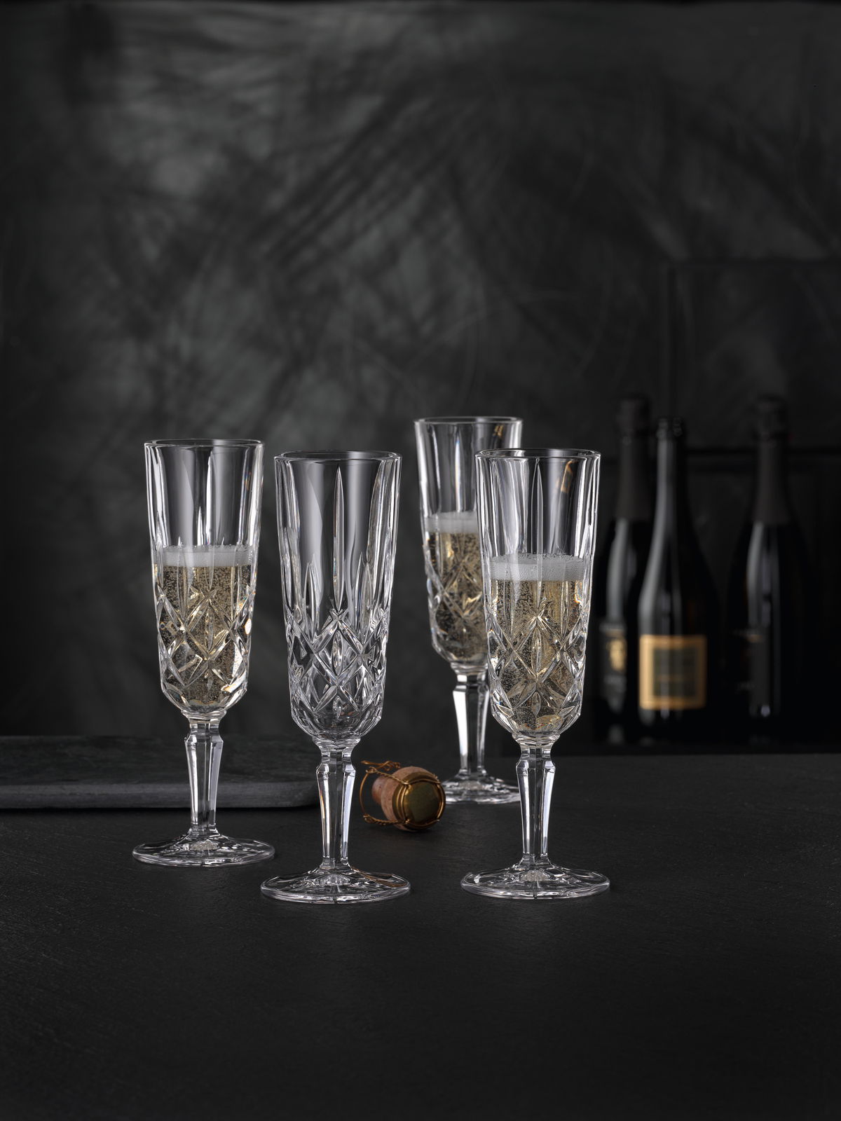 Vier elegante Champagnergläser Noblesse mit feinem Schliff, gefüllt mit Champagner, auf schwarzem Hintergrund. Perspektive von vorne.