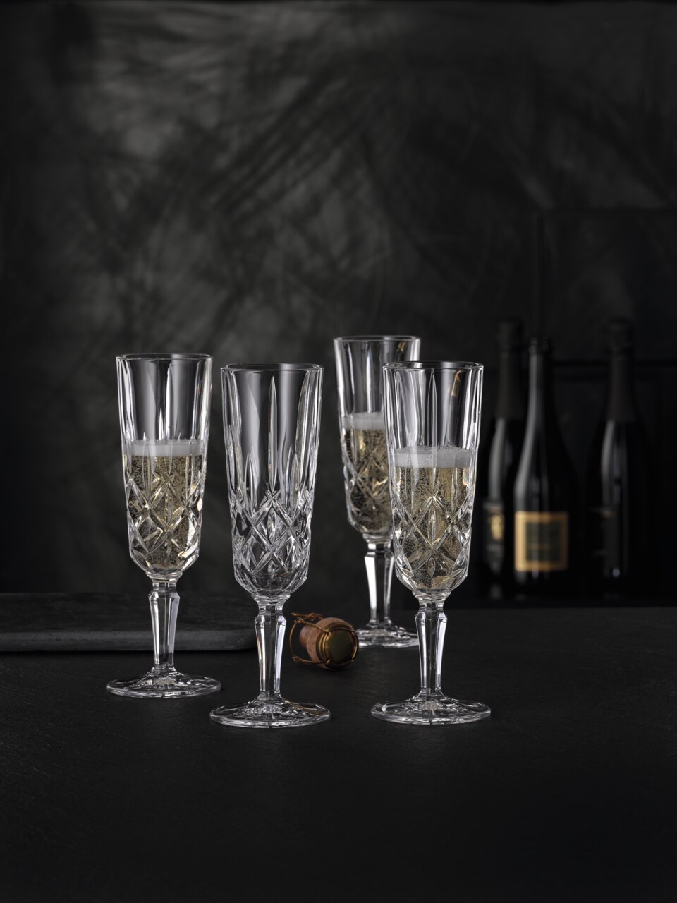 Vier elegante Champagnergläser Noblesse mit feinem Schliff, gefüllt mit Champagner, auf schwarzem Hintergrund. Perspektive von vorne.