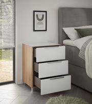 Moderne Nachtkommode mit drei offenen Schubladen, Holz- und Weißlack-Design, seitliche Perspektive neben einem Bett.