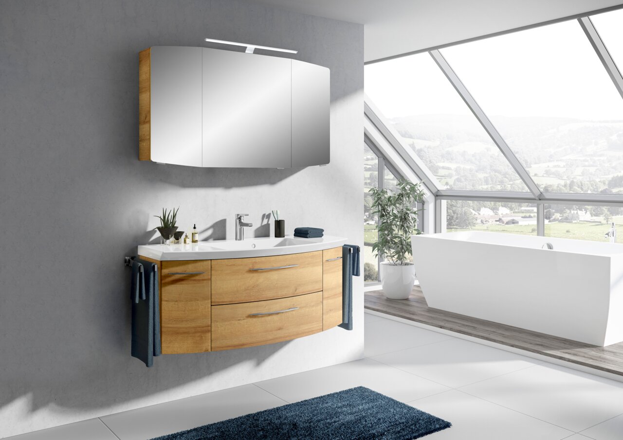 Moderne Badkombination mit Holzunterschrank und Spiegelschrank, seitliche Perspektive, in einem hellen Badezimmer mit großer Fensterfront.
