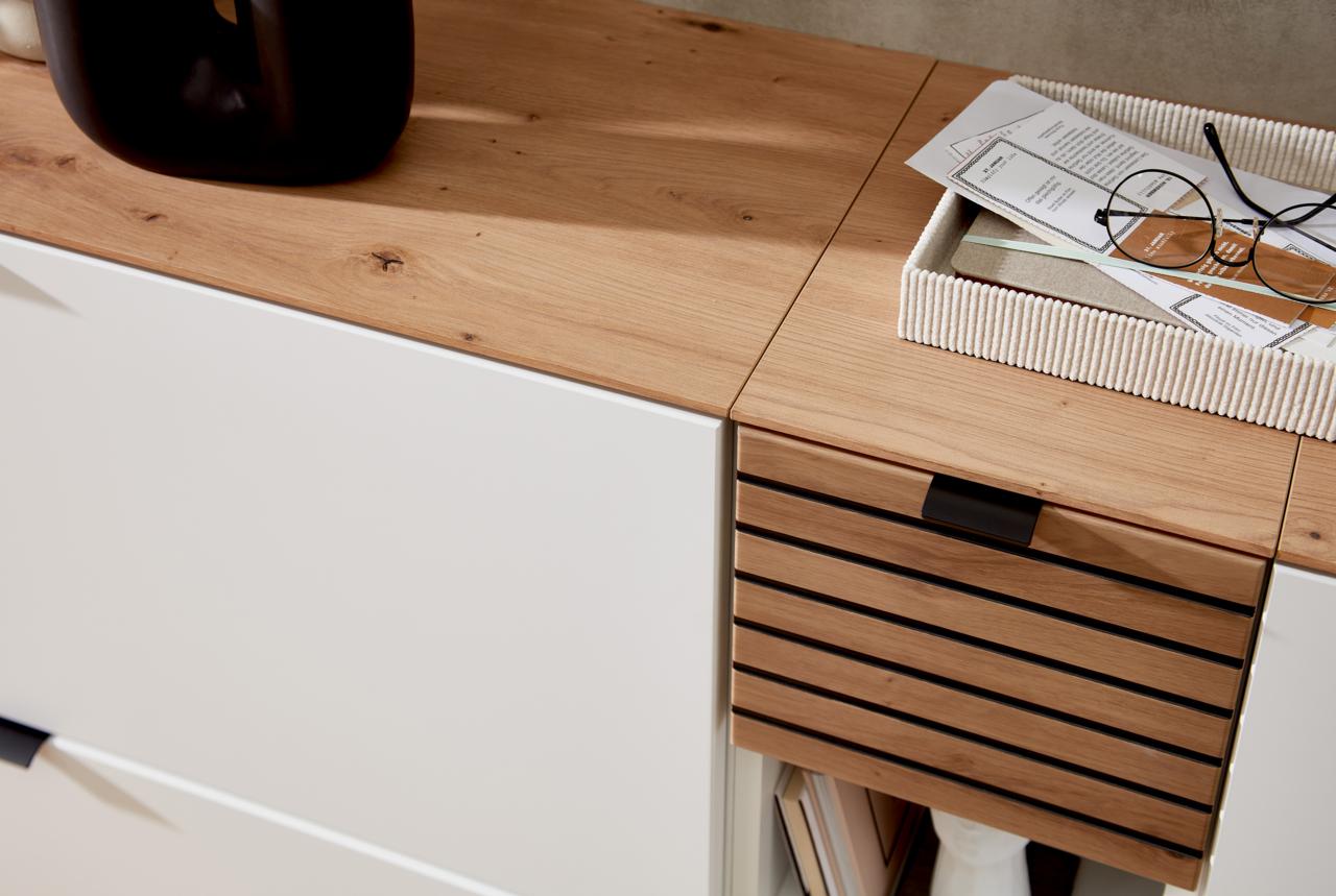 Nahaufnahme eines modernen Garderoben-Sets mit weißem und holzfarbenem Finish, von oben betrachtet. Auf der Oberfläche befinden sich Dekorationsgegenstände und eine Brille.