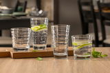 Vier Gläser mit strukturiertem Design, gefüllt mit Wasser, Limettenscheiben und Minzblättern, auf einem Holztisch in einer gemütlichen Esszimmerumgebung.