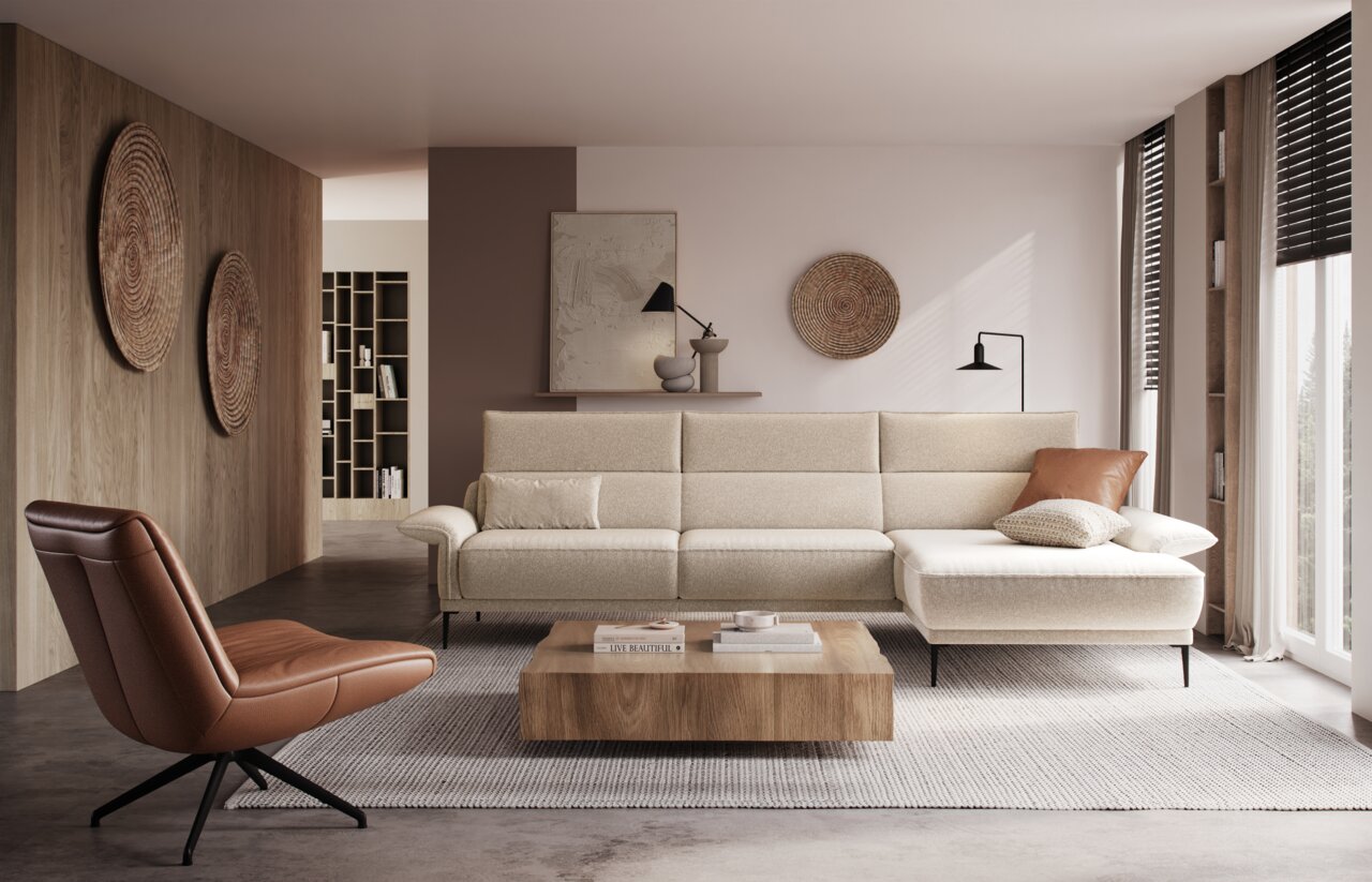 Modernes Wohnzimmer mit beiger Longchairkombination, frontal betrachtet. Die Couch ist mit Kissen dekoriert und steht auf einem Teppich. Ein brauner Sessel und ein Holztisch ergänzen das stilvolle Ambiente.